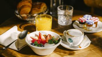 Ein Frühstückstisch mit Croissants, Orangensaft im Glas, Joghurt mit Früchten in einer Schale, einer Tasse Kaffee und einem Teller mit Gebäck.