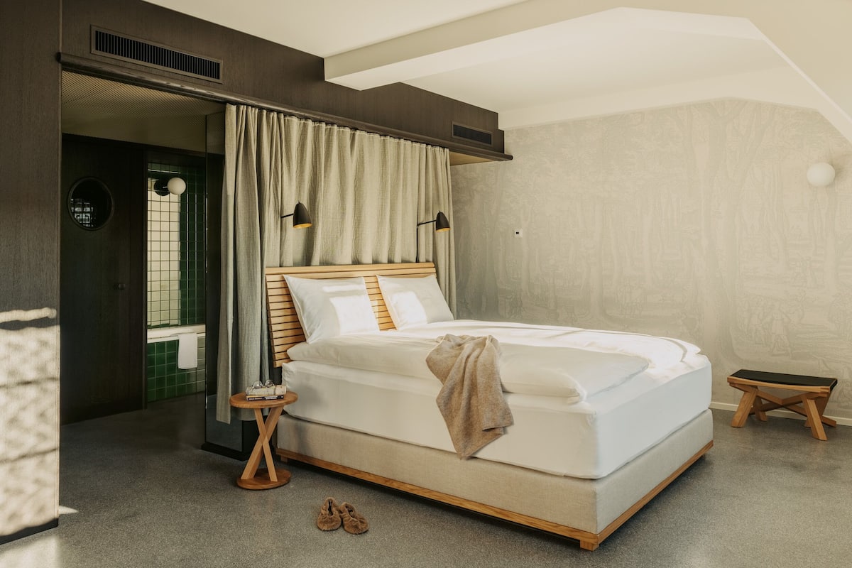 Un dormitorio moderno con una cama grande, una mesita de noche, un taburete pequeño y vistas al baño.
