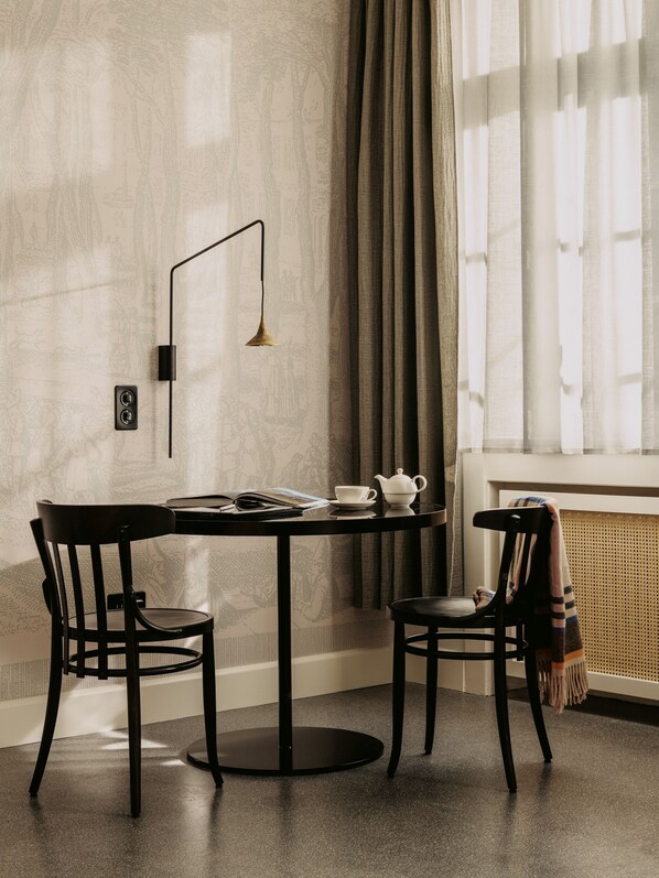 Una habitación moderna con una mesa redonda, dos sillas, una lámpara de pie y una ventana con cortinas.