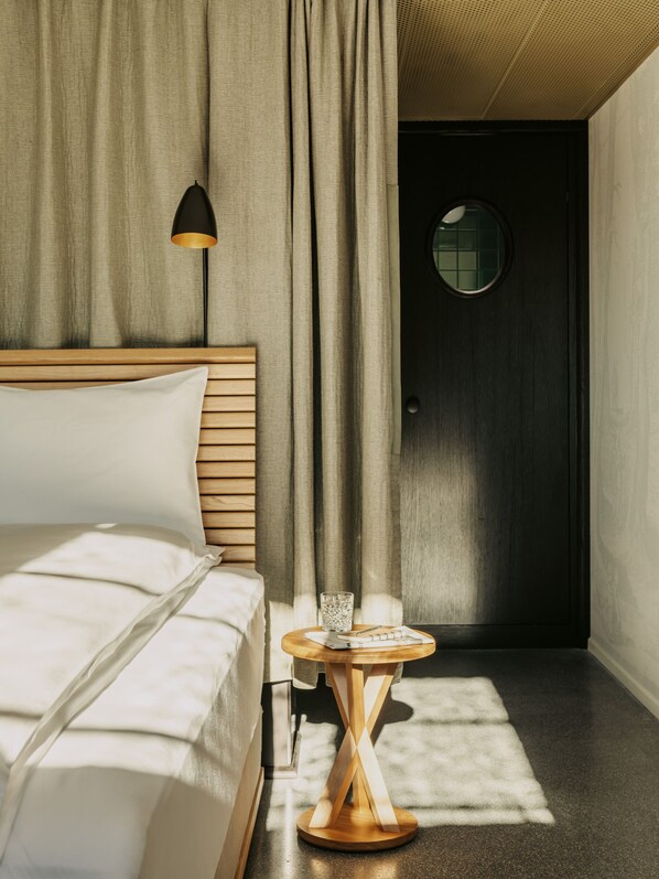 A modern hotel room with a wooden bed, a round table with a glass, and a dark door. - Boutique & Design Hotel Volkshaus Basel (Basel)