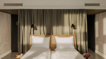 Una cama doble con cabecera de madera, dos mesitas de noche con libros y un gran ventanal con cortinas.