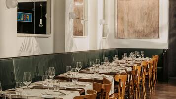Un restaurante con mesas de madera largas, manteles blancos y lámparas colgantes.