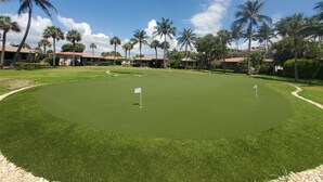 En golfbana med en puttinggreen, palmer och byggnader i bakgrunden.