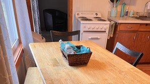 Une table de salle à manger en bois, avec des chaises, un panier, et un coin cuisine équipé d’une cuisinière et de placards.