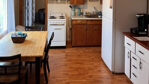 Une cuisine dotée de meubles en bois, d’un four à micro-ondes, d’une cuisinière, d’un réfrigérateur et d’une table à manger avec des chaises.