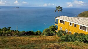 A yellow building with a balcony overlooking a coastal view. - Amazing views, relax far away from snow. Fantasy Vacation Planning Available. (St. Thomas)