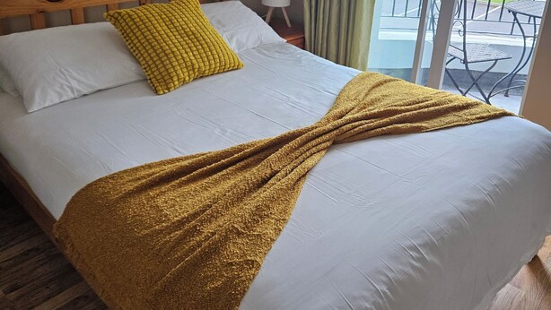 Une chambre d’hôtel avec un lit en bois, un oreiller jaune, une couverture blanche et une vue sur l’extérieur.