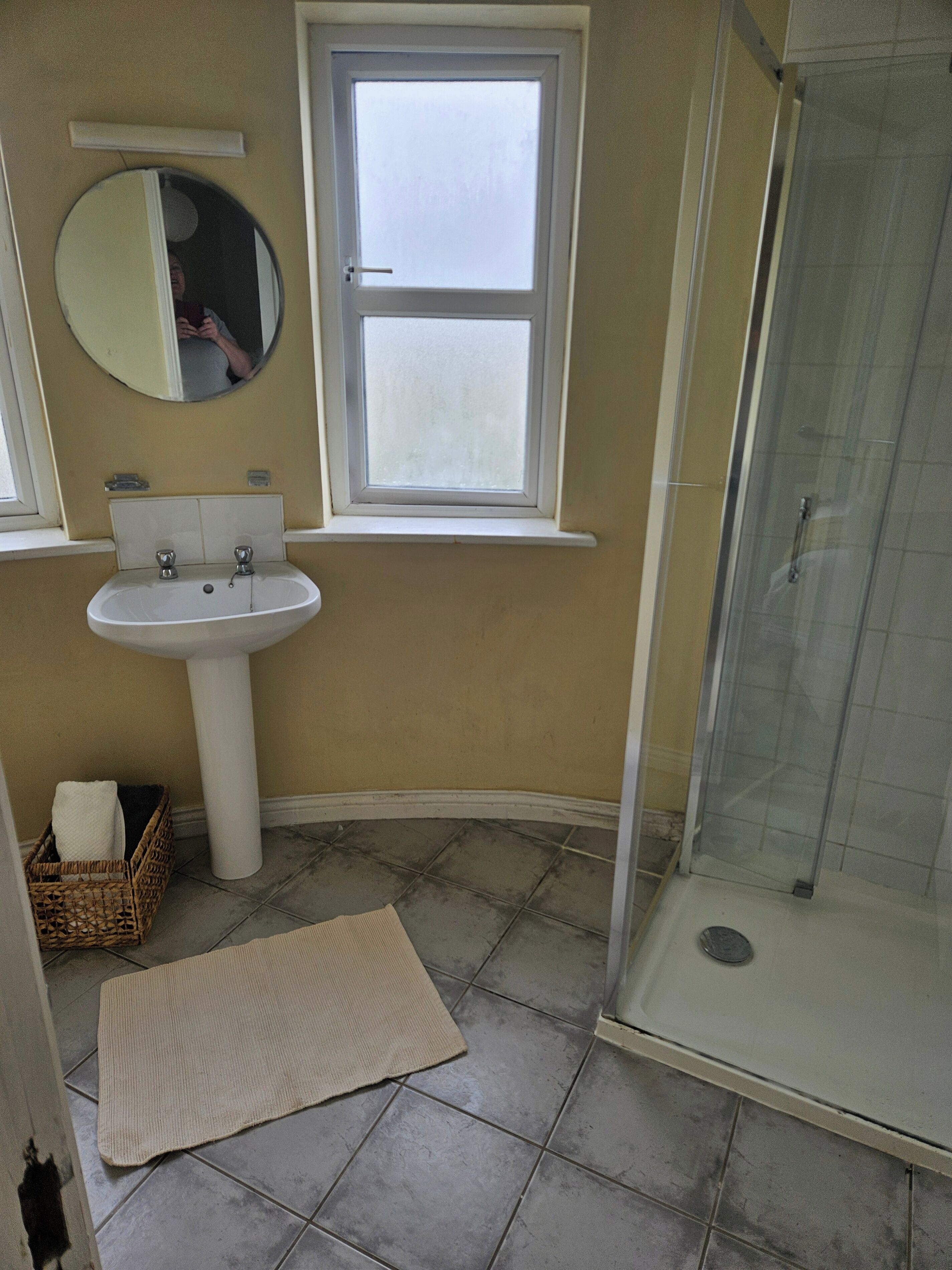 A bathroom with a sink, mirror, window, and shower.