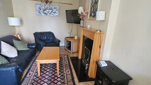 Un salon comprenant un canapé, une table basse, une cheminée, un téléviseur et un lustre.