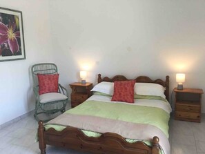 A bedroom with a wooden bed, two bedside tables with lamps, a green chair, and a floral painting on the wall.
