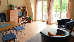 A living room with a TV, wooden cabinet, potted plant, and a dining area with chairs and a table.