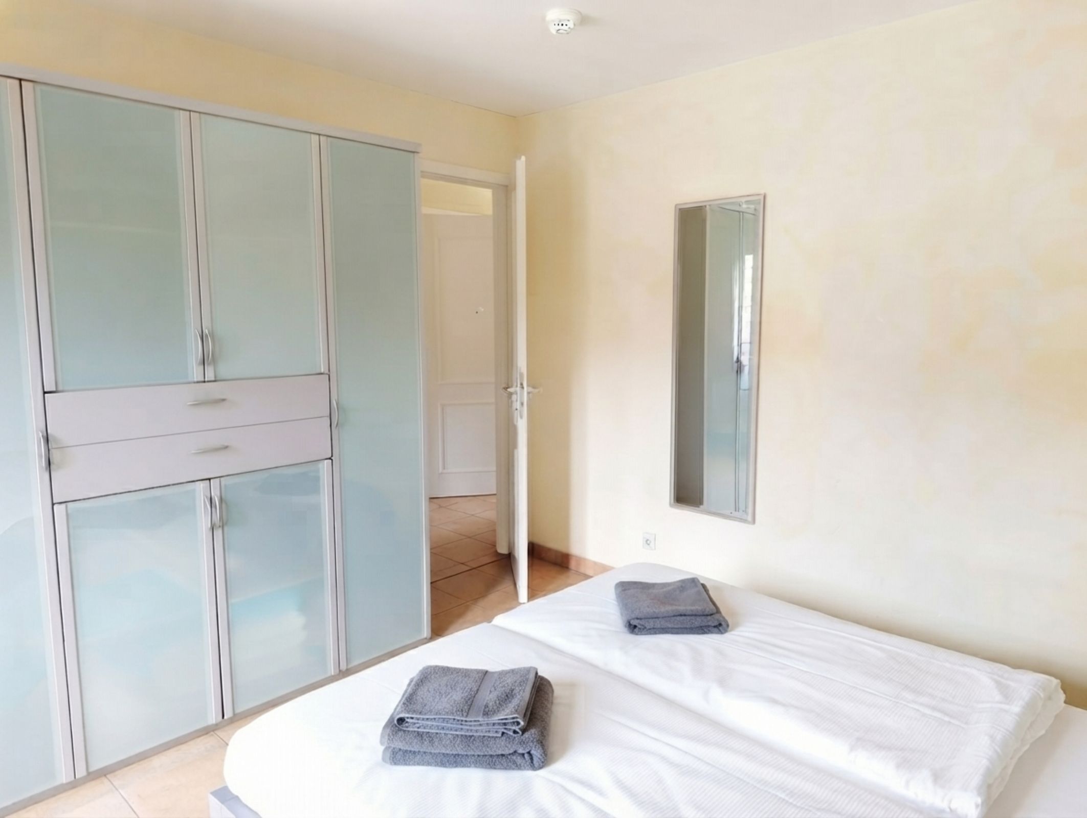 Ein Schlafzimmer mit einem Bett, zwei Handtüchern, einem Kleiderschrank und einem Spiegel.