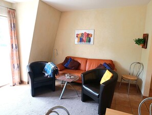 Un salon comprenant un canapé, deux fauteuils, une table basse et un tableau accroché au mur.