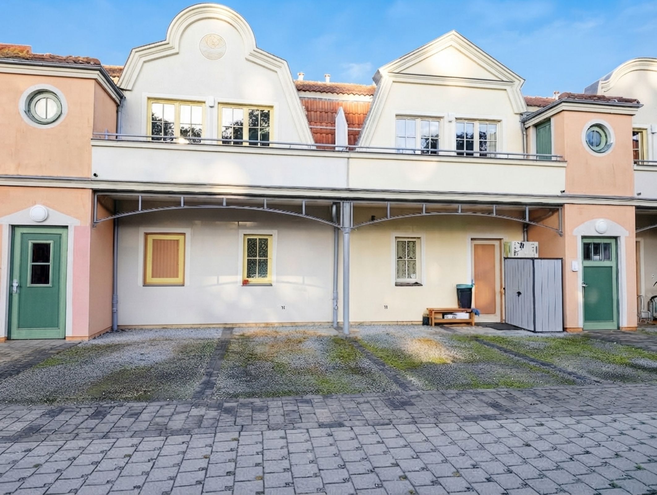 Ein zweistöckiges Gebäude mit einem zentralen Balkon, einer kleinen Bank und einem Mülleimer.
