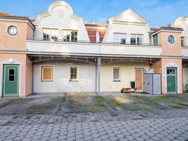 A two-story building with a central balcony, a small bench, and a trash bin.