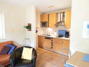 A compact kitchen with a microwave, stove, and sink, adjacent to a dining area with a table and chairs.