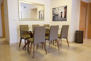 A dining area with a glass table and six chairs, a large mirror, and a framed picture on the wall.