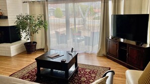 A living room with a fireplace, a large window with curtains, a television, and a potted plant. - Spacious centrally located peaceful house Red Rock views and a fenced dog yard! (Sedona)