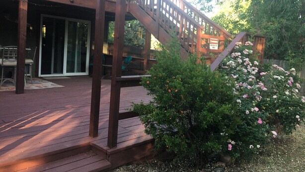 A wooden deck with a staircase leading to a covered area, surrounded by greenery and a sign indicating a restricted area. - Spacious centrally located peaceful house Red Rock views and a fenced dog yard! (Sedona)