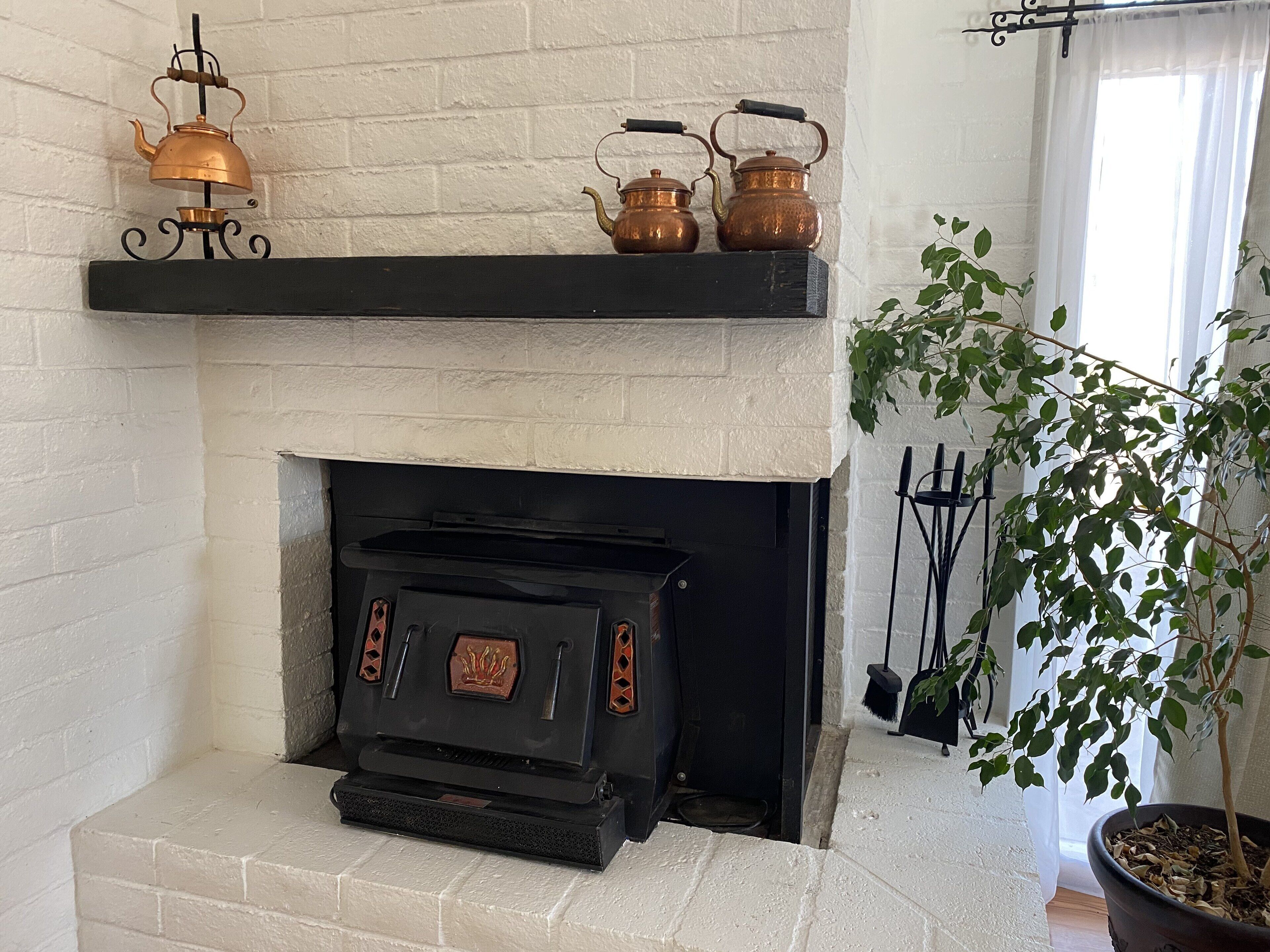 A fireplace with a black mantel, a decorative copper kettle, and a brass tea pot.