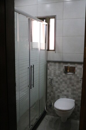 A bathroom with a glass-enclosed shower, a toilet, and a tiled wall.