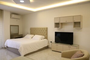 A modern hotel room with a large bed, a flat-screen TV, a sofa, and built-in cabinets.