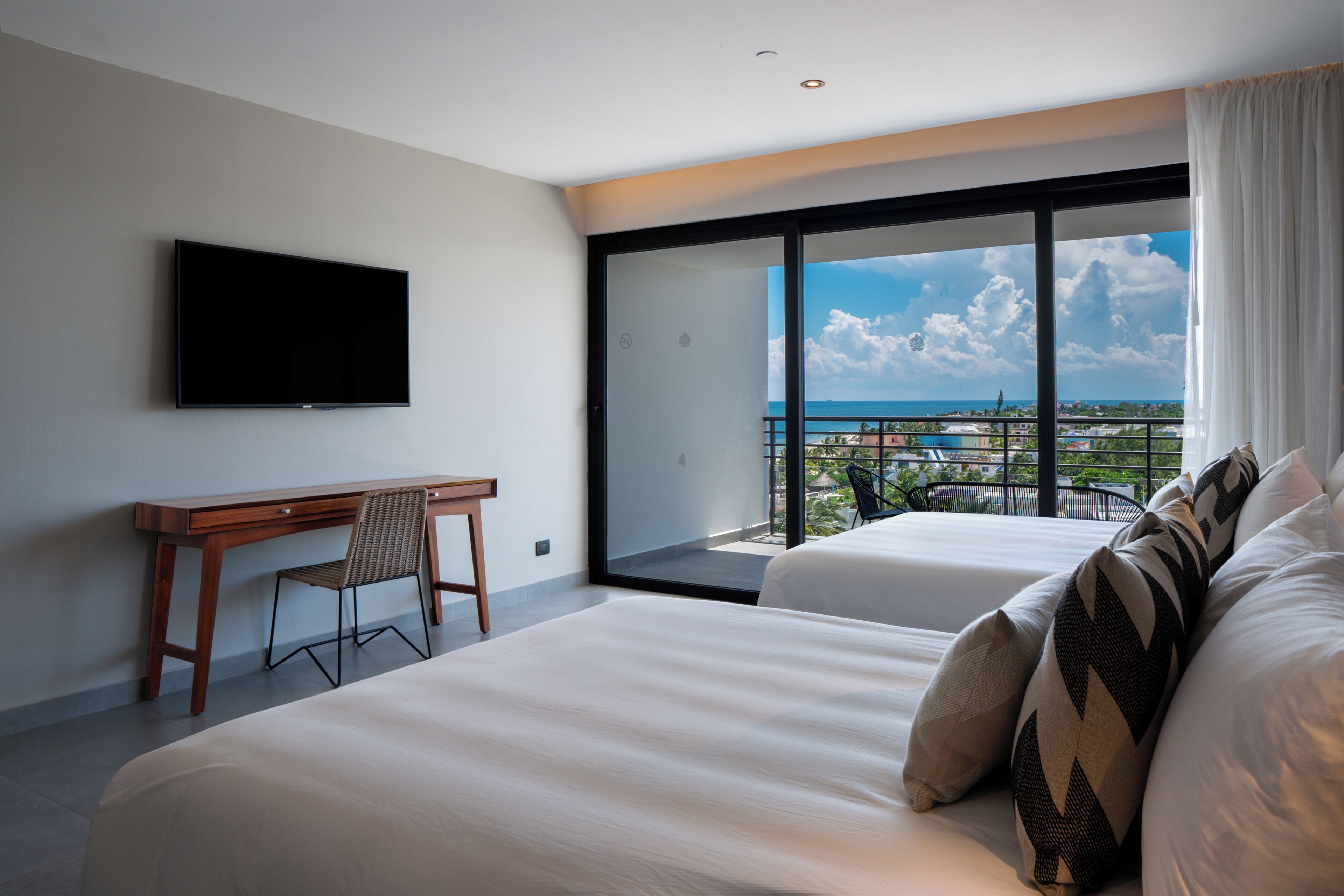 Une chambre d’hôtel avec un grand lit, un bureau et une télévision. Elle dispose d’un balcon avec vue sur la ville et l’océan.