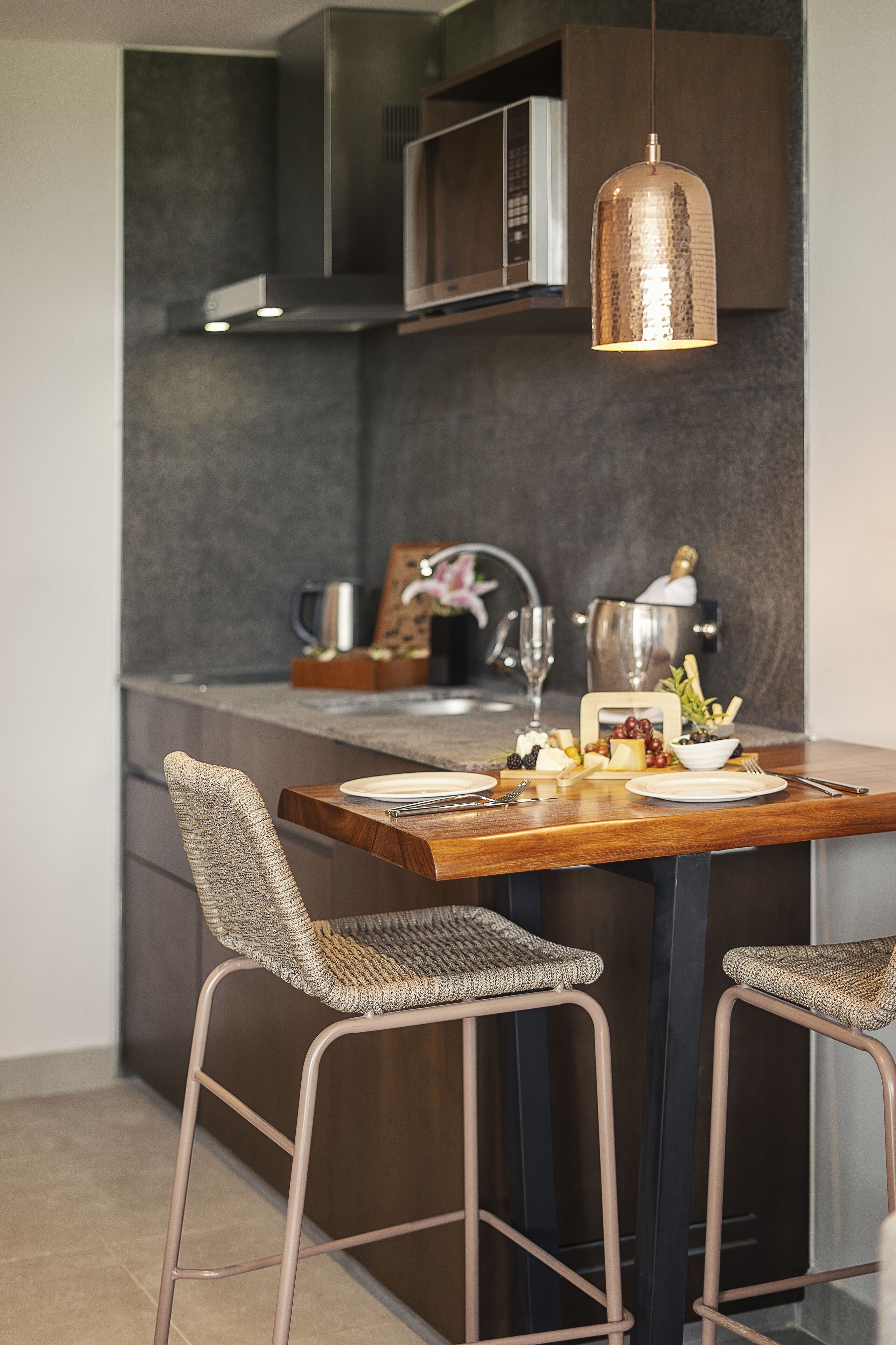 Una cocina moderna con una mesa de comedor de madera, dos taburetes de bar y una lámpara colgante.