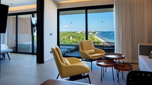 Une chambre d’hôtel moderne dotée d’un grand balcon, d’un canapé, de deux fauteuils et d’une table basse.