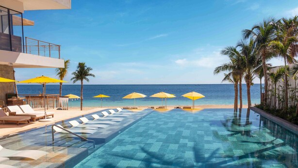 Un espace piscine avec une eau d’un bleu limpide, des chaises longues et des parasols jaunes.