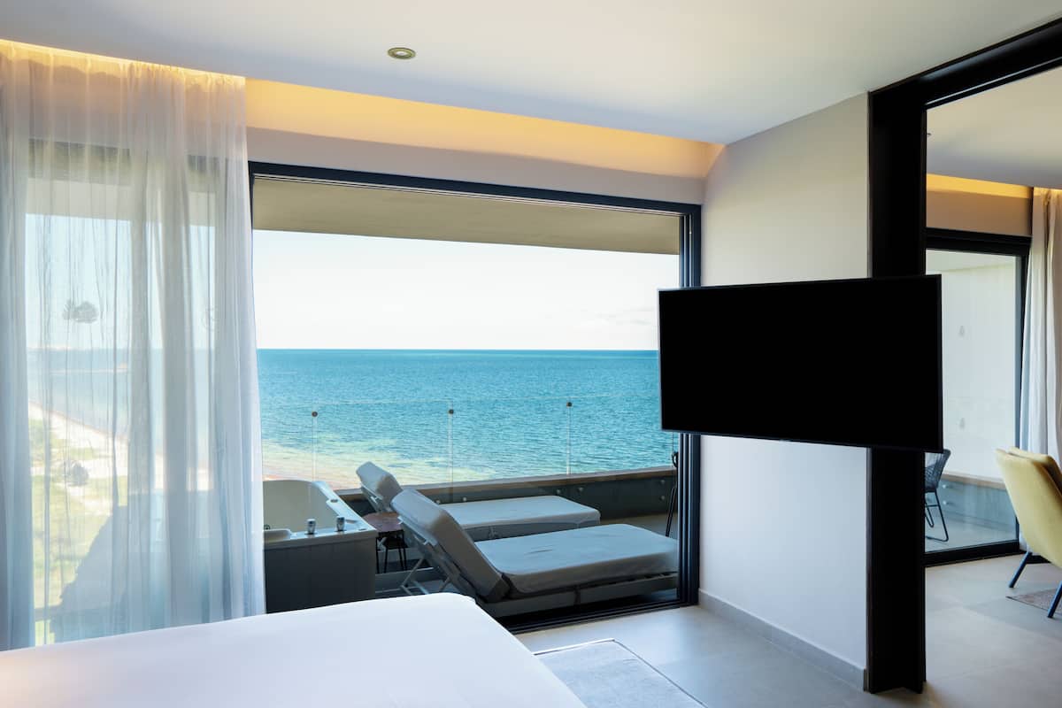 Une chambre d’hôtel moderne dotée d’un grand balcon, d’un lit, d’une télévision et offrant une vue sur la mer.