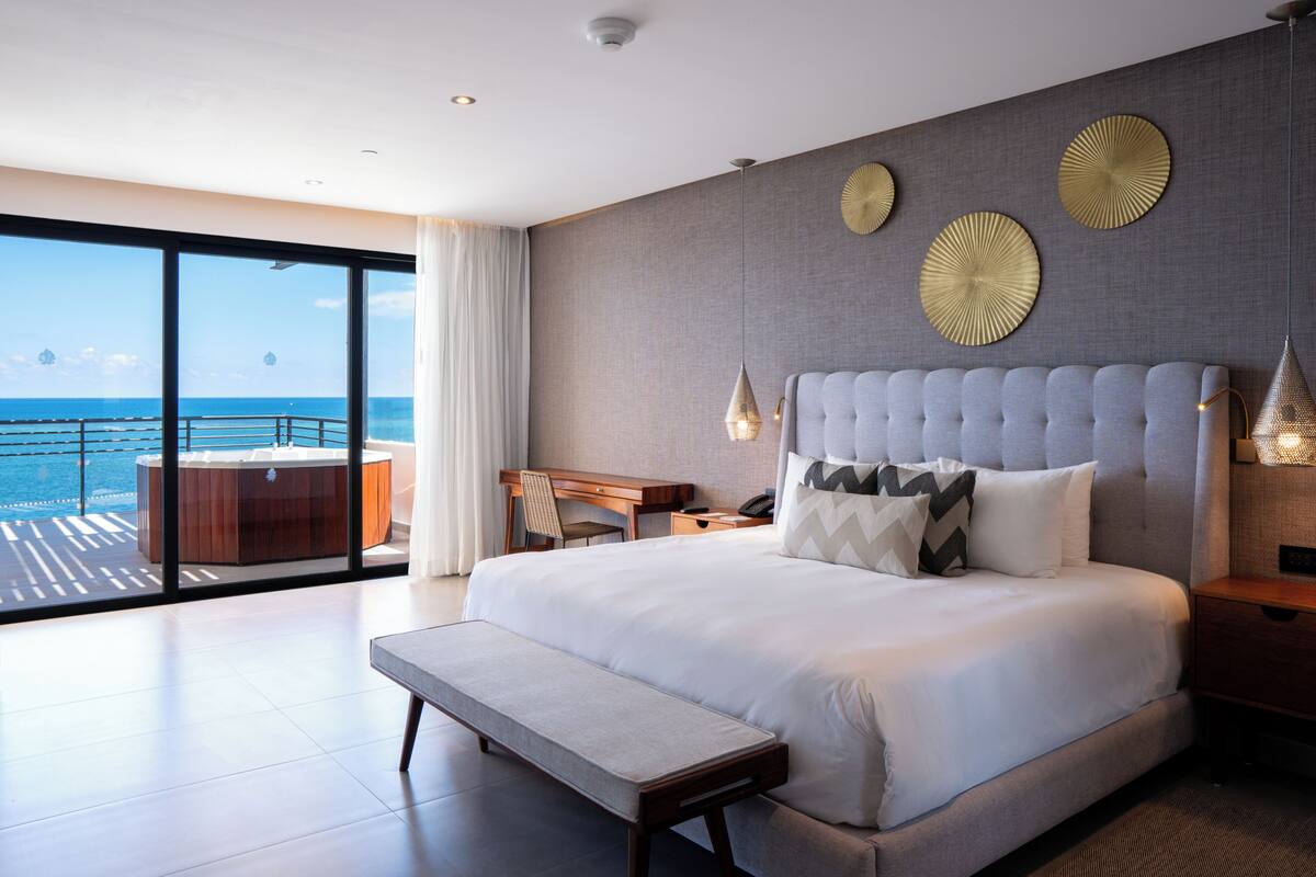 Une chambre d’hôtel moderne avec un grand lit, un bureau et une vue sur l’océan.