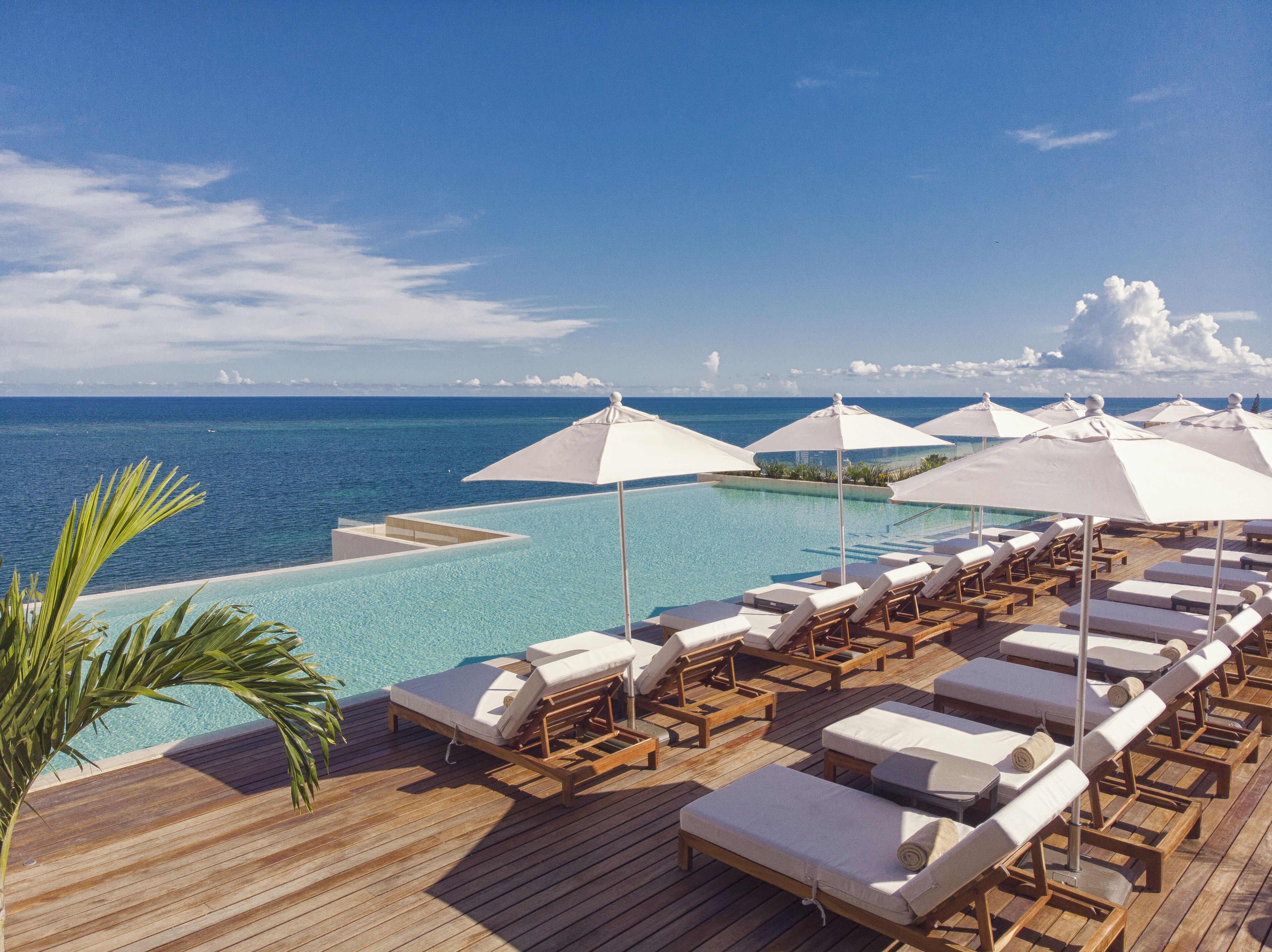 Zona piscina con poltronghe a sdraio e ombrelloni con vista su un mare blu e limpido.