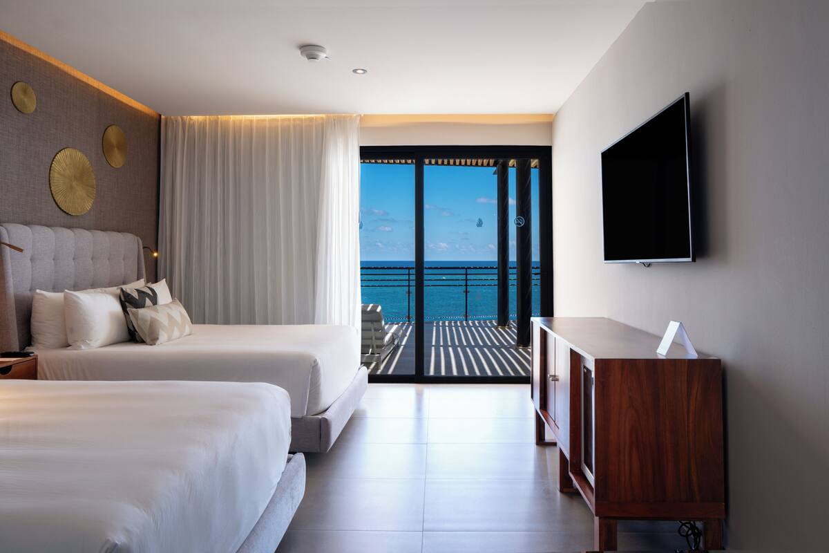 Une chambre d’hôtel avec deux lits, une télévision et un balcon donnant sur la mer.
