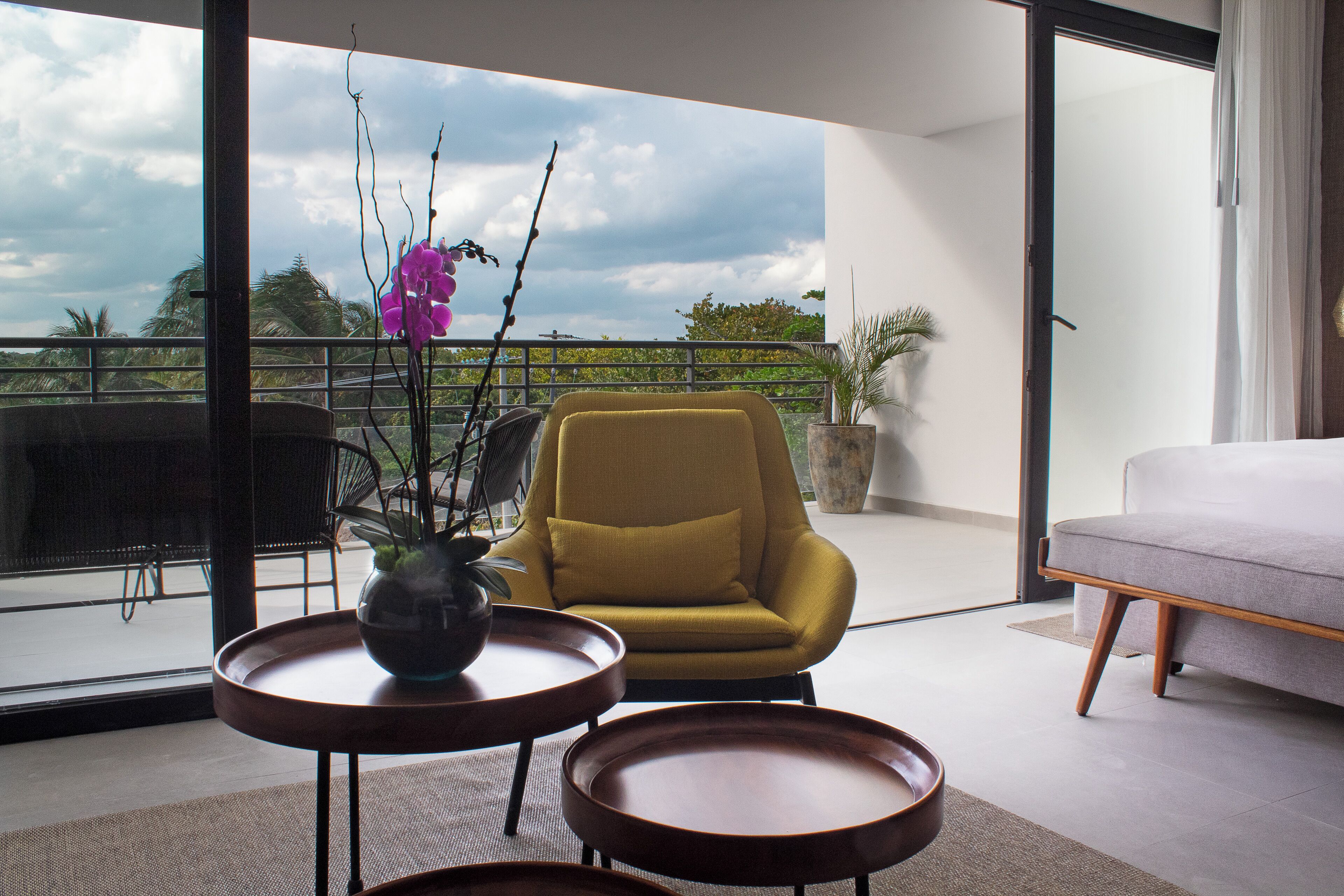 Een moderne woonkamer met een gele fauteuil, een bank en uitzicht op het buitengebied.