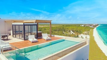 Ein moderner Infinity-Pool mit Glaskante, mit Blick auf einen Strand und den Ozean.