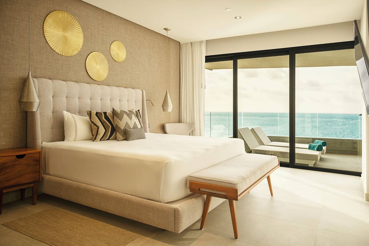 Une chambre spacieuse avec un grand lit, une vue sur l’océan et un balcon équipé de chaises longues.