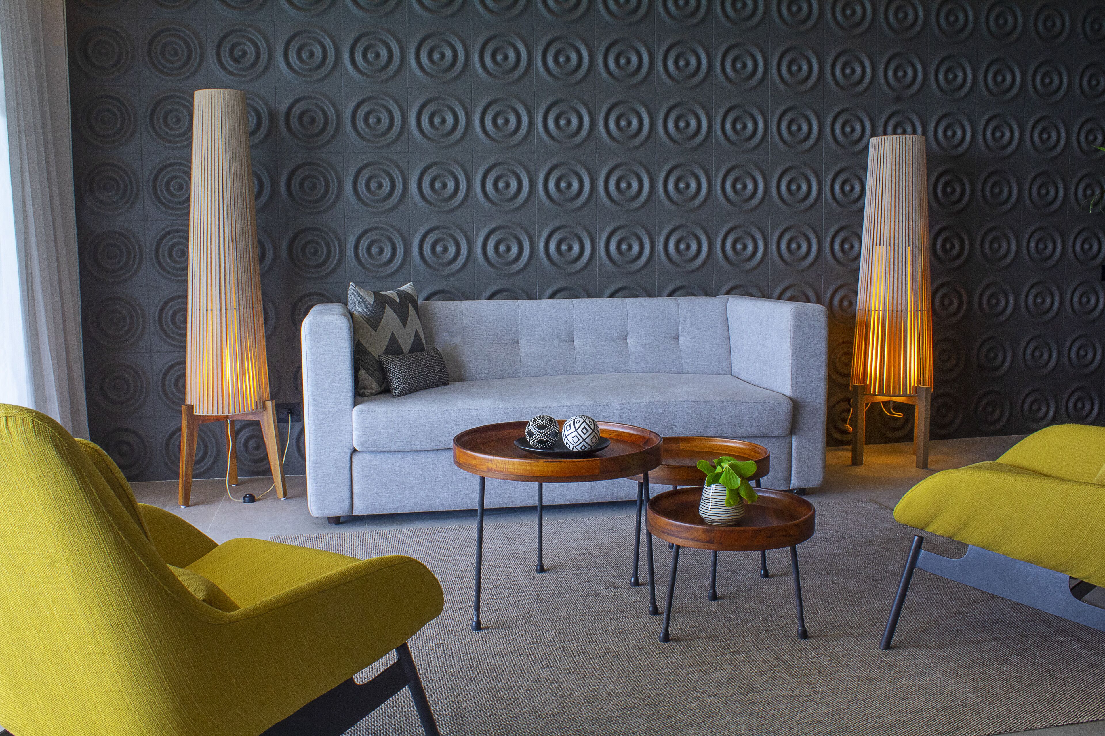 A modern living room with a grey sofa, yellow and green chairs, wooden side tables, and decorative lamps.