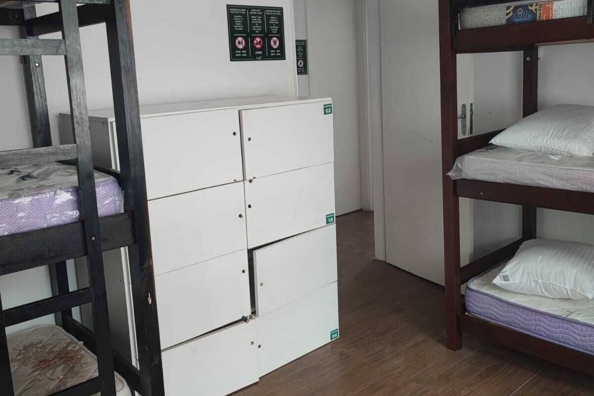 A dormitory room with bunk beds, a white wardrobe, and a small kitchenette.