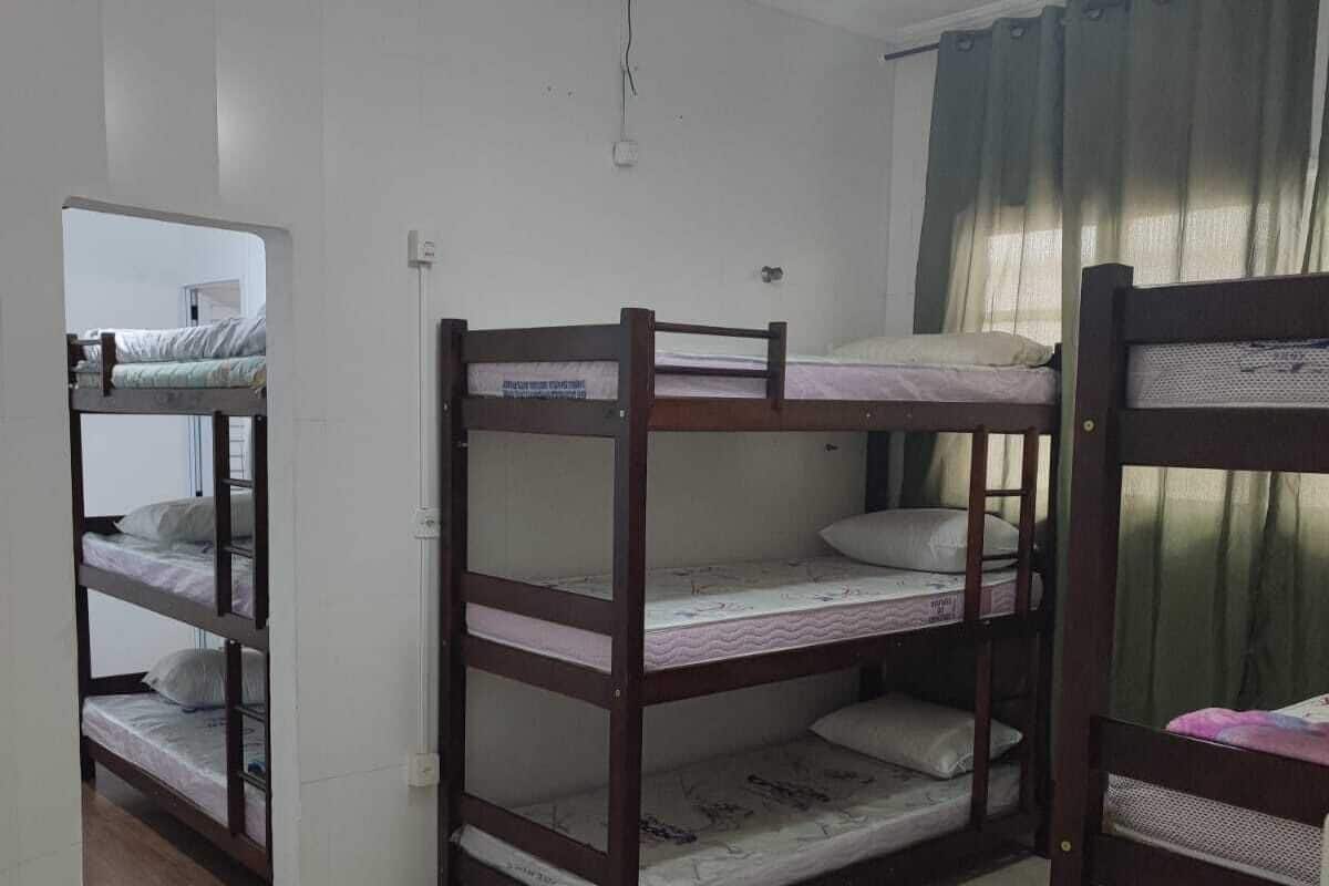A dormitory room with bunk beds, a ceiling fan, and a window with curtains.