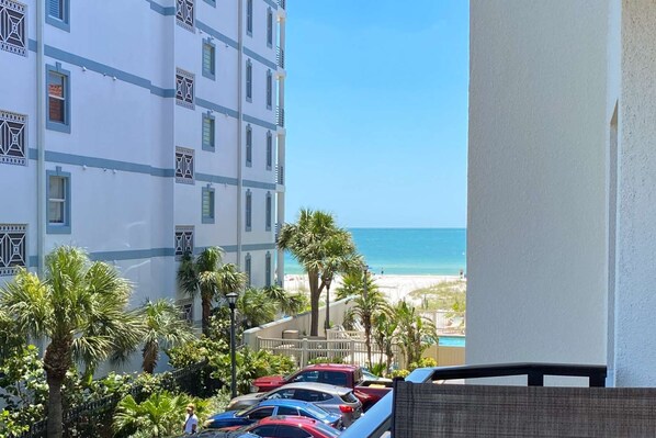 Vista de una playa desde un balcón, con coches aparcados y palmeras.