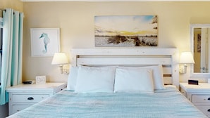 Une chambre à coucher avec un lit, deux tables de chevet, une commode, un tableau et un miroir.