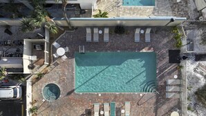 Vue aérienne d’un hôtel doté d’une grande piscine rectangulaire, de plusieurs chaises longues et d’un jacuzzi circulaire.