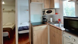 A compact kitchenette with a microwave, coffee maker, and washing machine. There is a bed and a small table in the adjacent sleeping area. - REDUCTIONS : TO RENT MOBILE HOME IN LA COTINIERE (Saint-Pierre-d'Oléron)