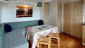 A cozy room with a wooden ceiling, a sofa, a table with a tablecloth, and a chair. - REDUCTIONS : TO RENT MOBILE HOME IN LA COTINIERE (Saint-Pierre-d'Oléron)