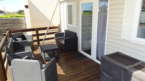 A covered outdoor area with wicker furniture, a wooden deck, and a sliding glass door leading to a covered porch. - REDUCTIONS : TO RENT MOBILE HOME IN LA COTINIERE (Saint-Pierre-d'Oléron)