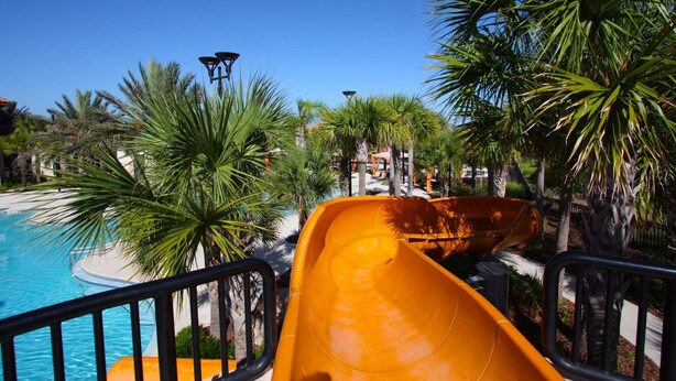A water slide at a resort with a pool and palm trees. - 5BR Solterra Disney Retreat w/ Themed Rooms | Tall Ceilings | Game Room | Large pool and spa (Davenport)