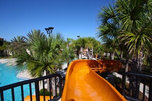 Un tobogán de agua en un resort con piscina y palmeras.