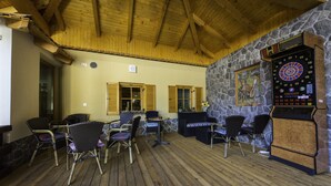 A covered outdoor seating area with wooden flooring, stone walls, and a dartboard. - Guesthouse Vodnik (Cerklje na Gorenjskem)