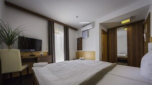 A hotel room with a bed, a desk with a television, a chair, a potted plant, and a mirror. - Guesthouse Vodnik (Cerklje na Gorenjskem)